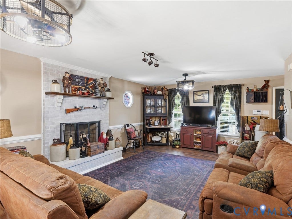6723 Bull Hill Road, Prince George, VA 23875 Painted brick fireplace featuring a wood mantel, octagonal window, two metal-frame drum chandeliers, and wood-finish flooring