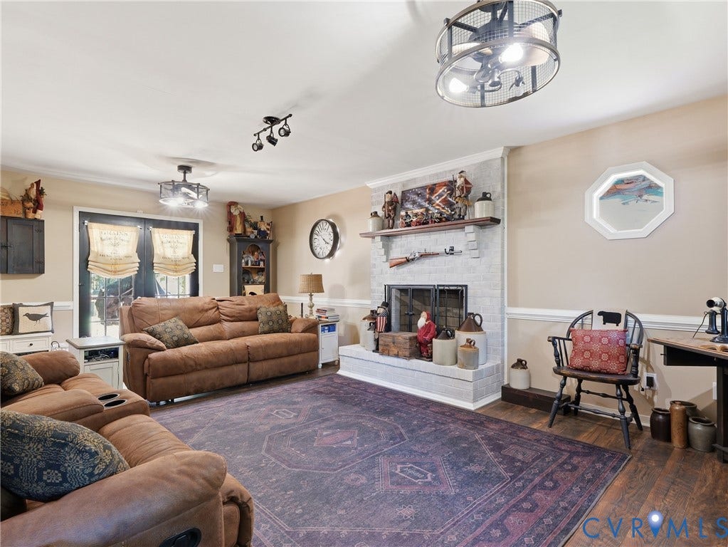 6723 Bull Hill Road, Prince George, VA 23875 Light-toned brick fireplace with a wood mantel, dark wood-finish flooring, dual industrial-style cage ceiling light fixtures, and glass-paned double doors