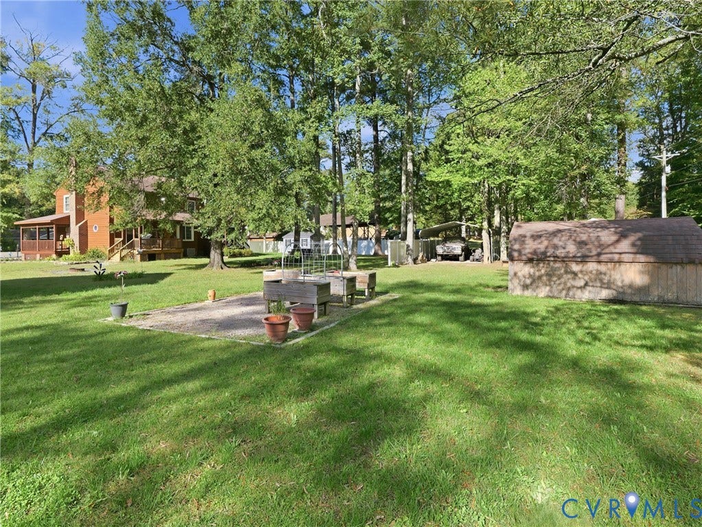 6723 Bull Hill Road, Prince George, VA 23875 Expansive lawn featuring mature trees, a gravel-based garden area with raised wood planter boxes, a detached storage structure, and a covered parking area