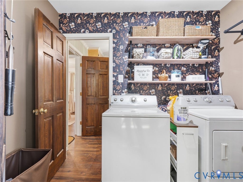 6723 Bull Hill Road, Prince George, VA 23875 Laundry area featuring wood-finish flooring, decorative floral wall covering, and built-in industrial-style shelving with wood surfaces and black metal supports, complemented by solid wood doors