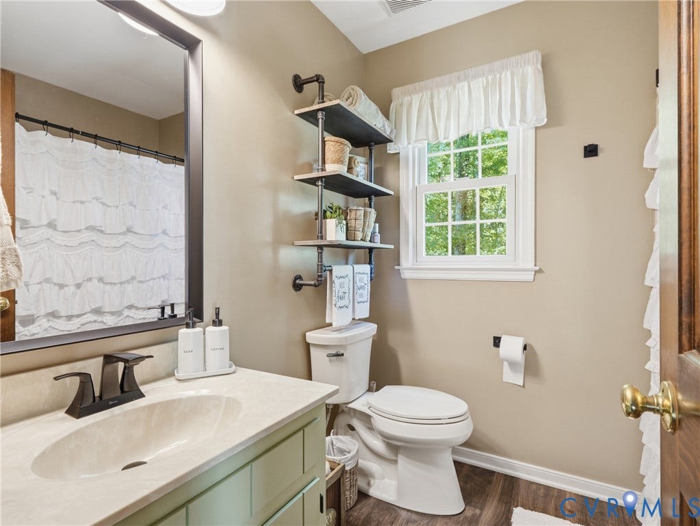 6723 Bull Hill Road, Prince George, VA 23875 Vanity with an integrated sink and light-toned solid surface countertop, matte black faucet, framed mirror, industrial-style pipe shelving, and wood-finish flooring