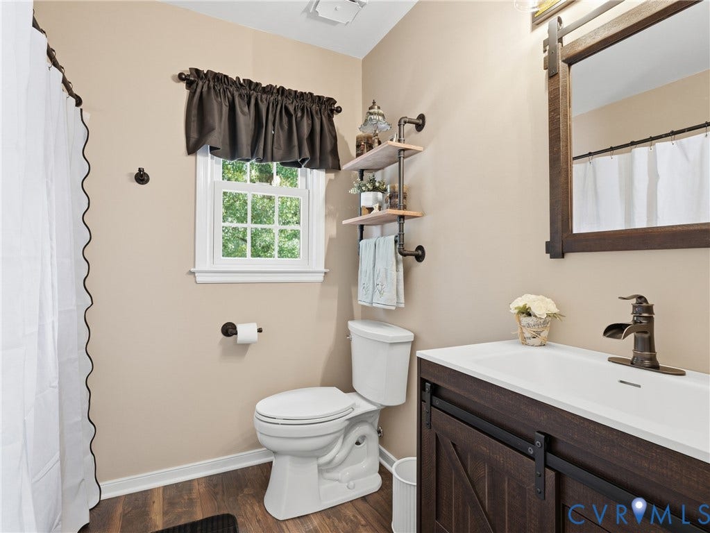 6723 Bull Hill Road, Prince George, VA 23875 Bathroom featuring a wood-finish vanity with a white integrated sink, oil-rubbed bronze faucet, rustic wood-framed mirror, and wall-mounted industrial pipe shelving