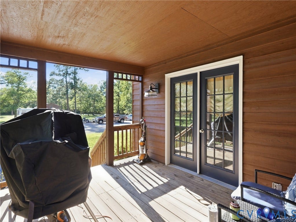 6723 Bull Hill Road, Prince George, VA 23875 Covered porch featuring wood-finish siding, wood decking, glass-paneled double doors, and an attached exterior wall-mounted light fixture