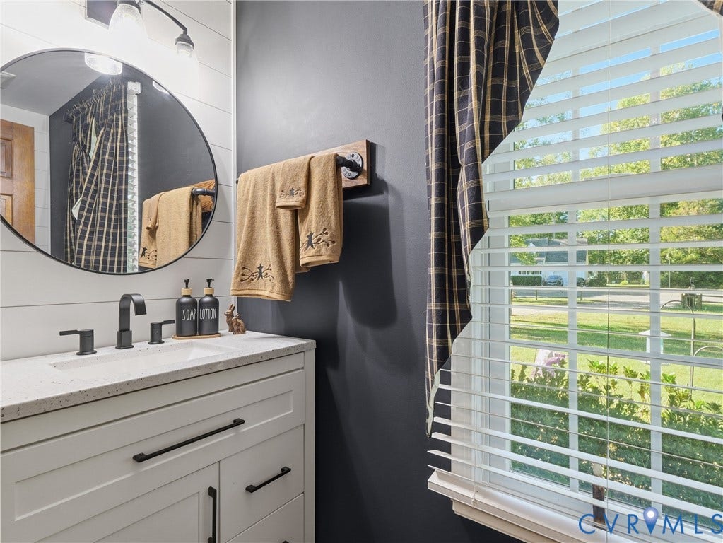 6723 Bull Hill Road, Prince George, VA 23875 White vanity featuring a stone-composite countertop, undermount sink, and matte black hardware, accented by shiplap wall detailing, a circular mirror, and industrial-style metal pipe fixtures