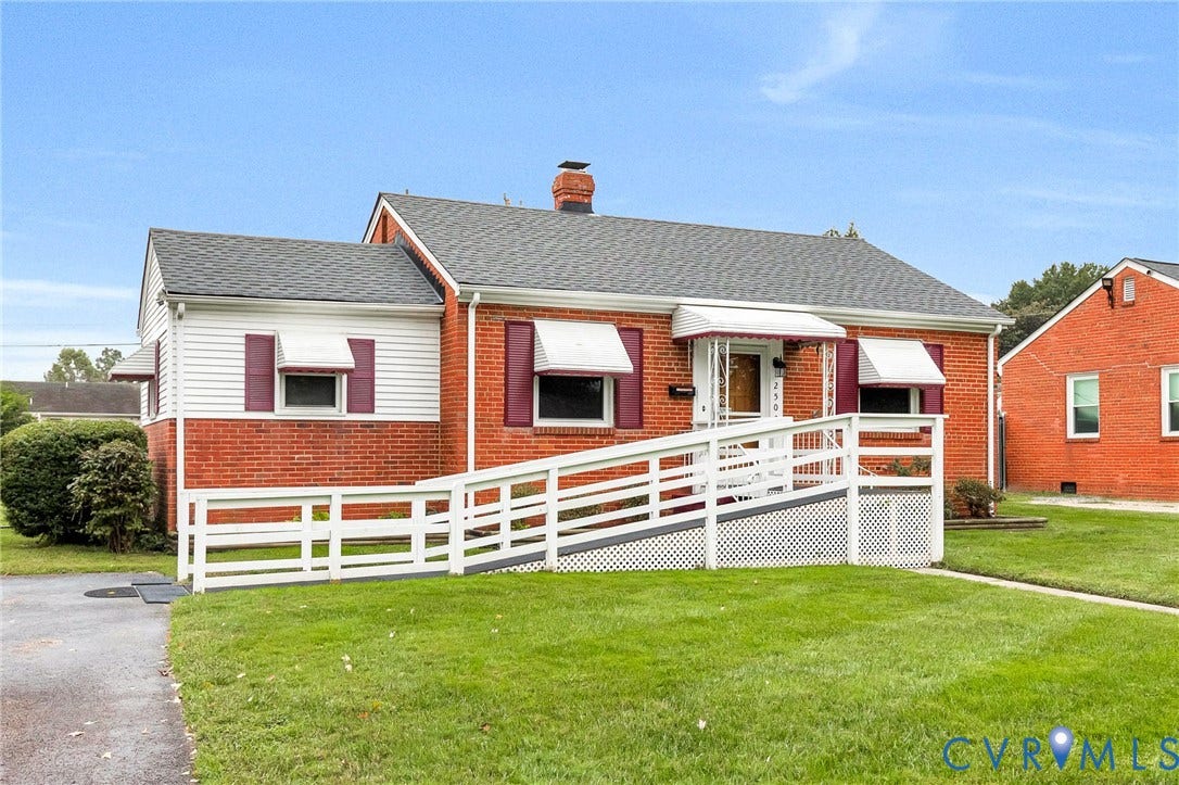 2503 Carlisle Avenue, Henrico, VA 23231 Charming brick ranch home featuring a welcoming front porch with white railings and columns, multiple windows with white trim, a pitched roof with asphalt shingles, and a manicured lawn with mature landscaping