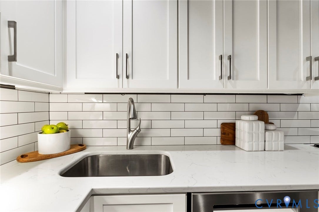 2714 E Broad Street, Church Hill, Richmond, VA 23223 White shaker-style cabinetry with dark hardware, white subway tile backsplash, stainless steel sink with gooseneck faucet, light-toned countertop, and stainless steel appliance