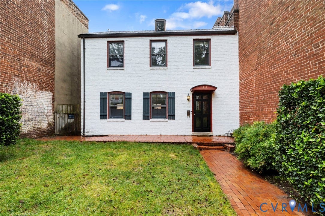 2714 E Broad Street, Church Hill, Richmond, VA 23223 White brick exterior with a black front door, featuring dark window shutters, an arched entryway awning, and a brick pathway