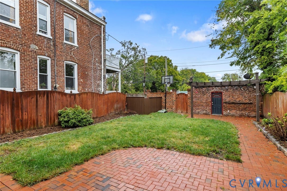 2714 E Broad Street, Church Hill, Richmond, VA 23223 Brick exterior with multiple windows, wooden privacy fence, established brick patio, and a separate brick structure with a dark door and overhead pergola