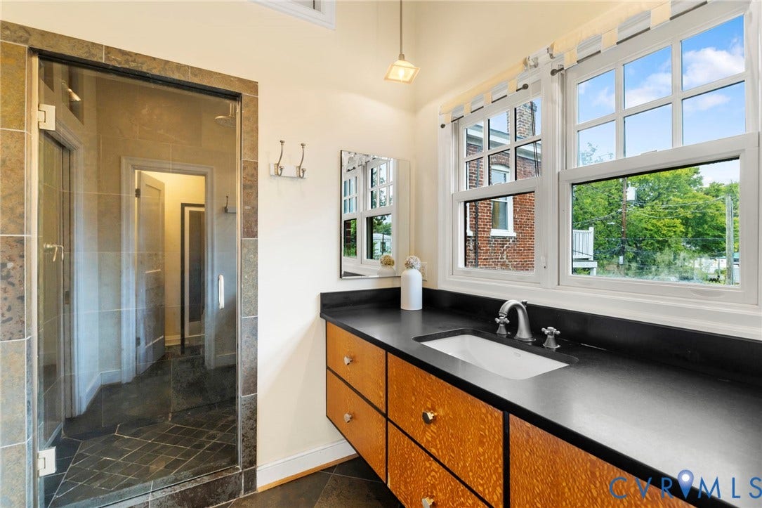 2714 E Broad Street, Church Hill, Richmond, VA 23223 Frosted glass shower enclosure, wood-finish vanity with drawer storage, dark countertop, and large white-framed windows