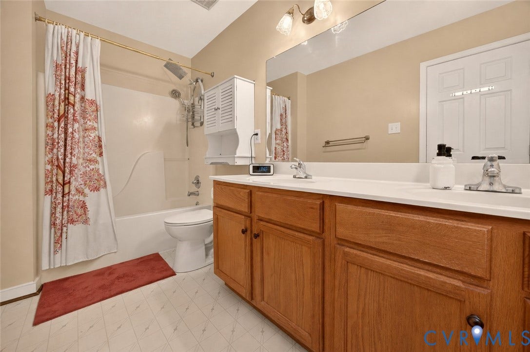 9516 Hungary Woods Drive, Henrico, VA 23060 Wood-finish vanity with dual sinks and white countertops, large wall-mounted mirror, and a full bathtub with shower