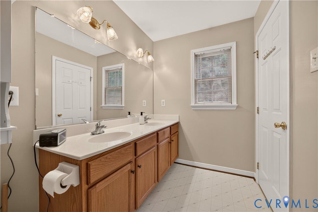 9516 Hungary Woods Drive, Henrico, VA 23060 Dual vanity with integrated sinks, wood-finish cabinetry, and an expansive wall-mounted mirror
