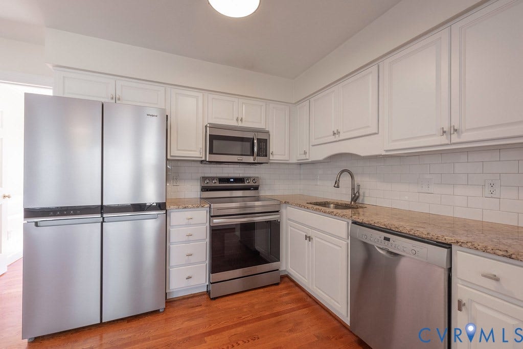 Kitchen featuring white cabinetry, stainless appliances, subway tile backsplash, and hardwood flooring