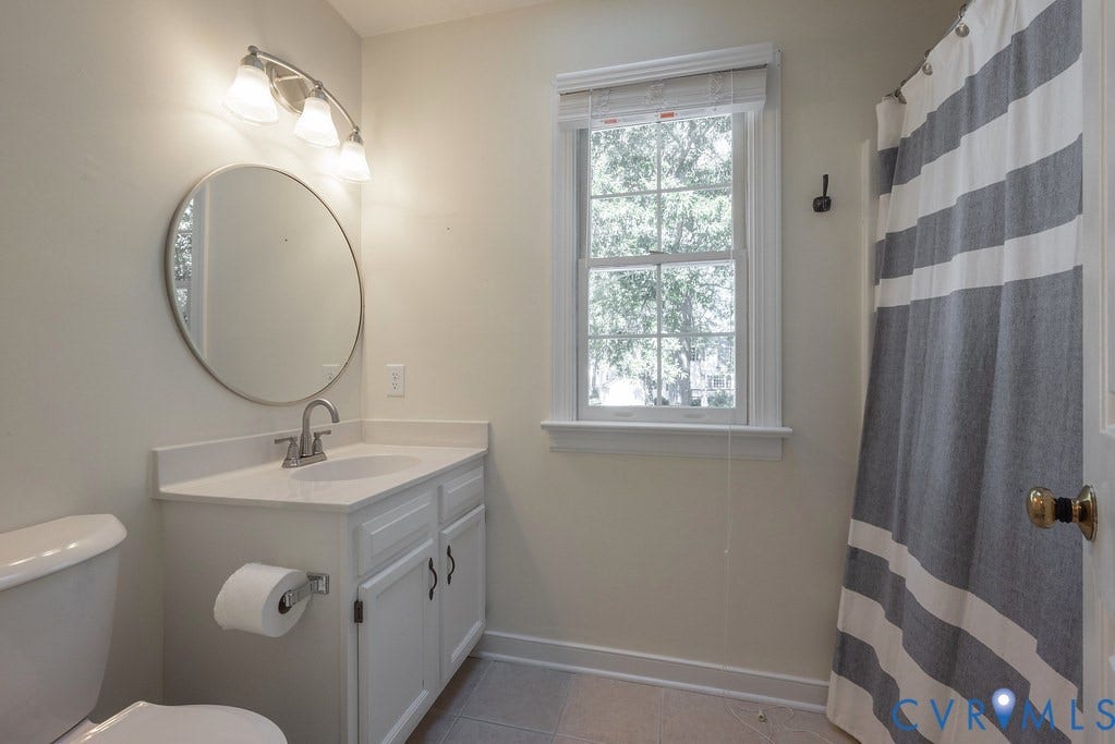 Bathroom featuring a vanity with white cabinetry, a circular mirror, and a window with natural light