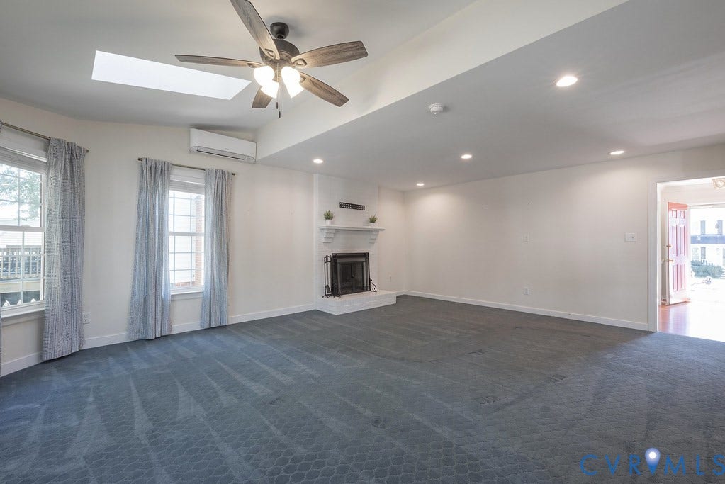Spacious room featuring a white brick fireplace with a mantel, multiple recessed lights,  skylights