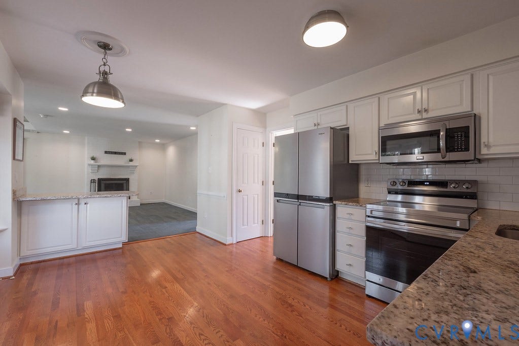 Kitchen featuring hardwood flooring, white cabinetry, granite countertops, and stainless appliances