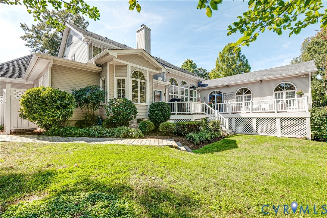 Exterior featuring a multi-level deck with white railings, arched windows, and mature landscaping