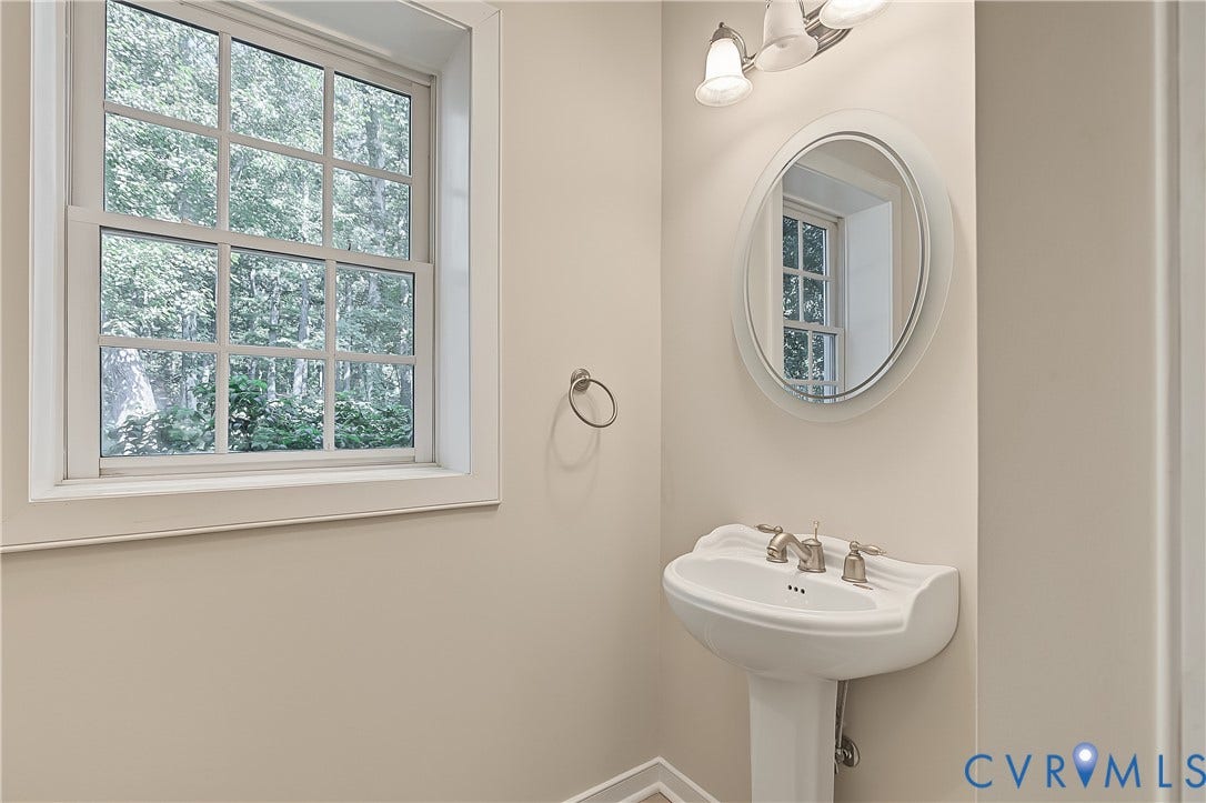Pedestal sink with brushed nickel faucet, wall-mounted mirror, and window with white trim