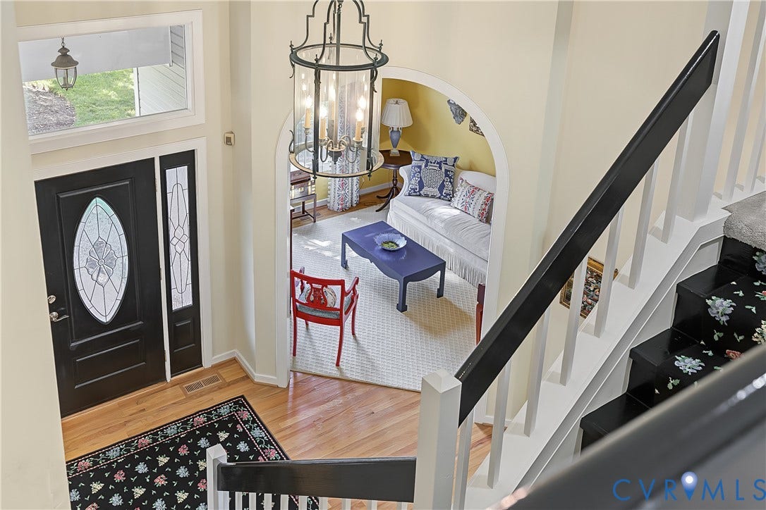 Two-story foyer with hardwood flooring, elegant chandelier, black front door with decorative glass inserts and a sidelight