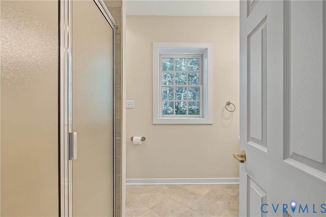 Enclosed shower with frosted glass, tiled flooring, and a paneled white door with brass hardware