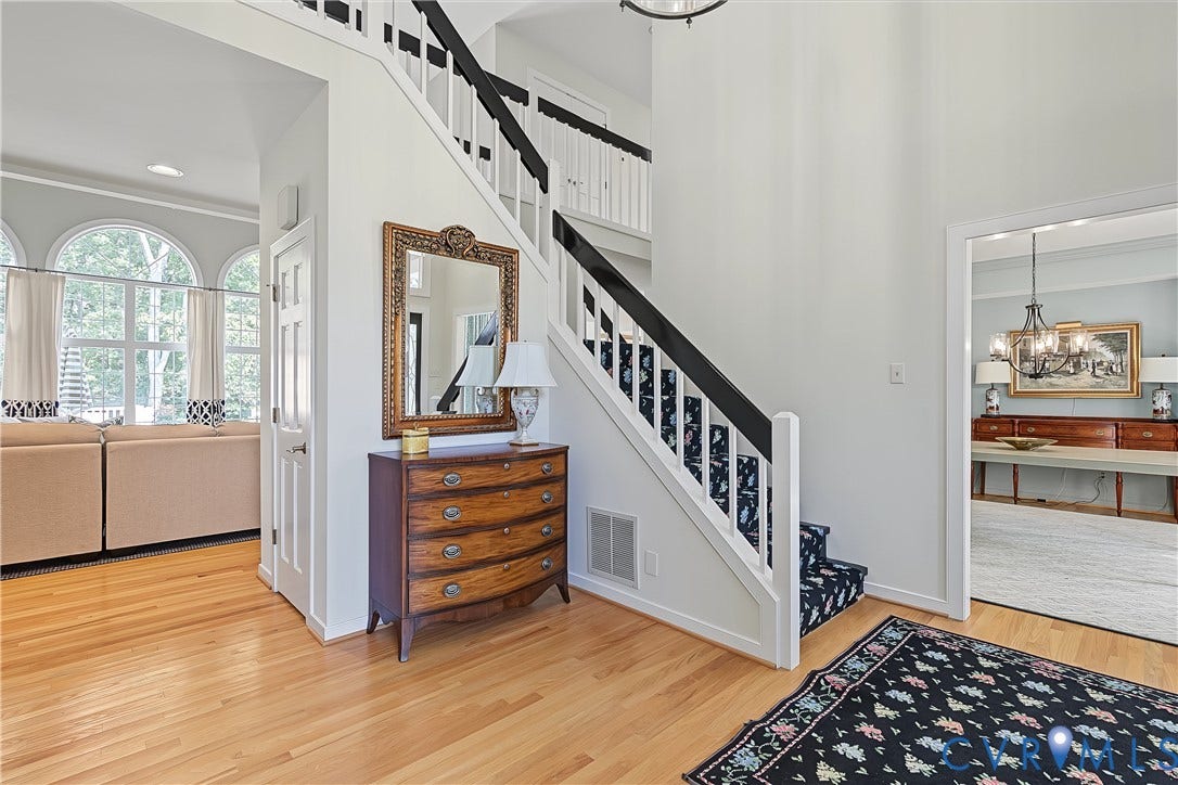 Hardwood flooring, white painted walls, white trim, and a white staircase with black handrails and a patterned runner