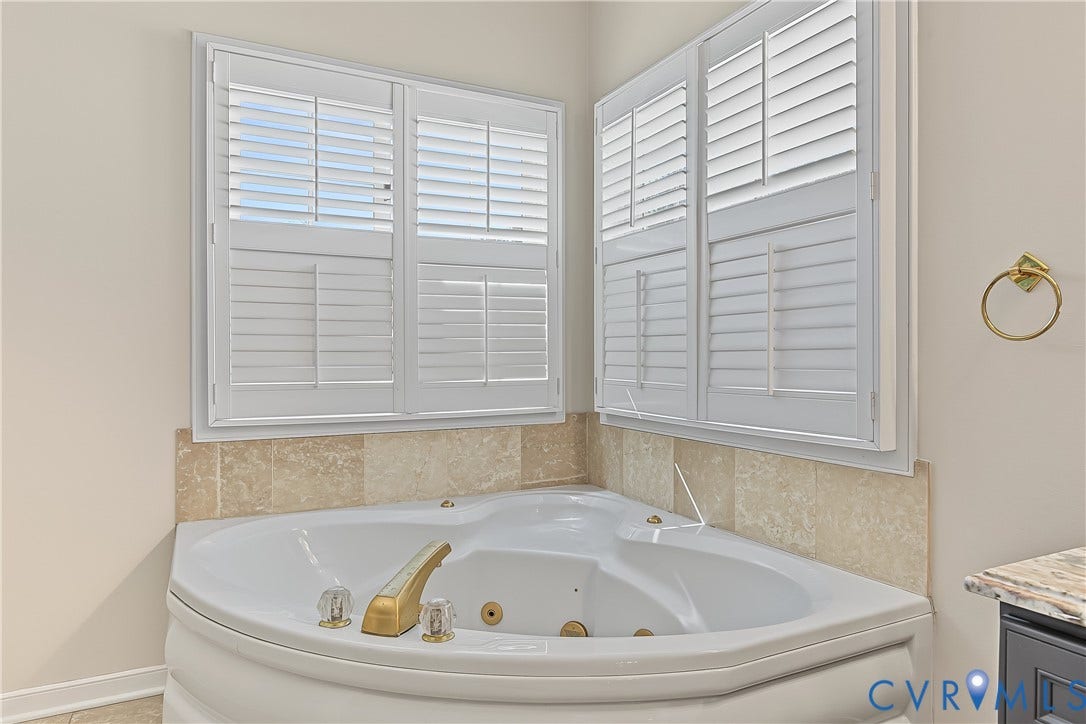 Corner soaking tub with integrated jets, featuring gold-toned fixtures and surrounding tile accents