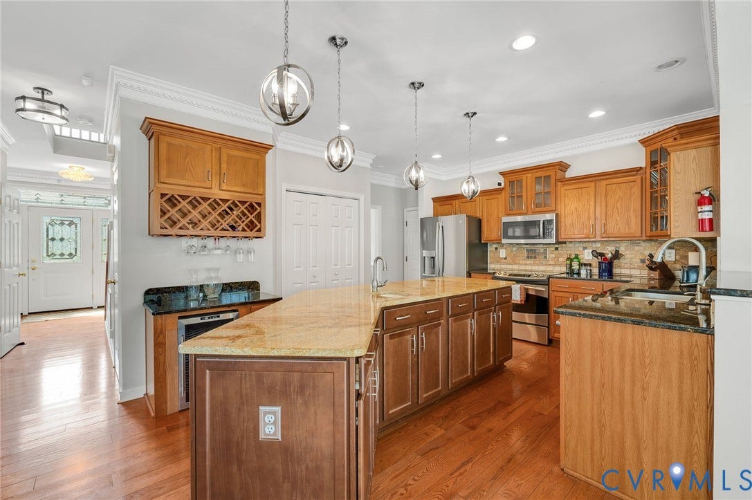 10808 Pruett Lane, Henrico, VA 23059 Kitchen featuring wood-finish flooring, an expansive island with a light-toned countertop, stainless steel appliances, and wood cabinetry with a built-in wine rack