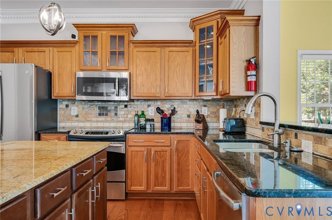10808 Pruett Lane, Henrico, VA 23059 Chef's kitchen featuring warm wood cabinetry with glass-front upper cabinets, stainless steel appliances including a gas cooktop, dual granite countertops with waterfall island seating, and a professional-style faucet with pull-down sprayer