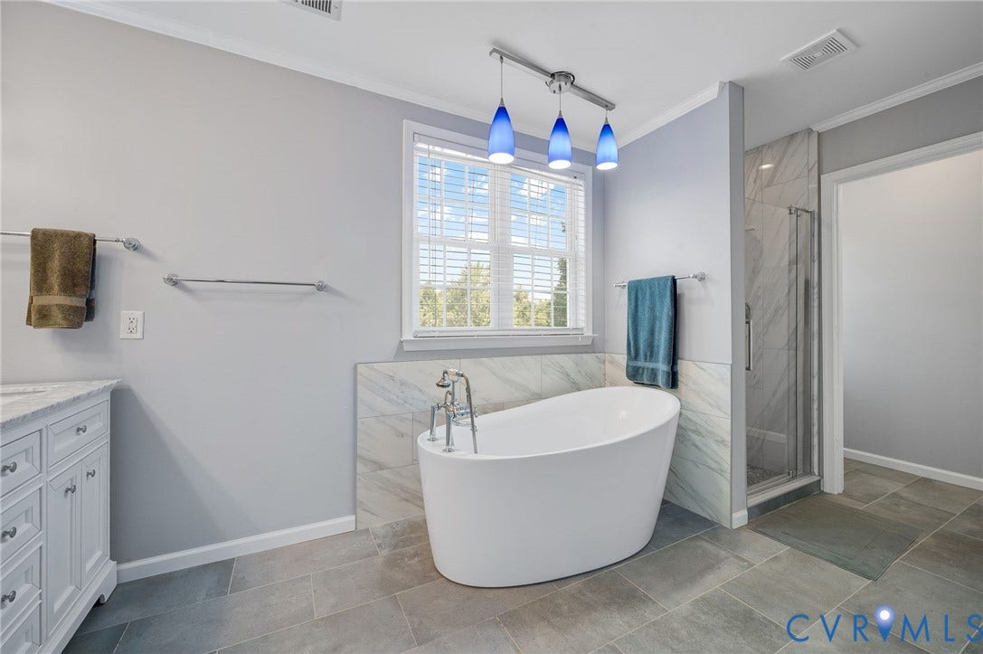 10808 Pruett Lane, Henrico, VA 23059 Freestanding soaking tub with floor-mounted fixtures, glass-enclosed shower with tiled surround, single vanity with light-colored countertop, and large format floor tiling
