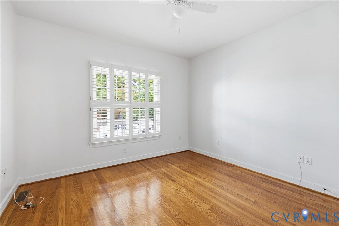 Hardwood flooring, white walls, window with white plantation shutters, and a ceiling fan