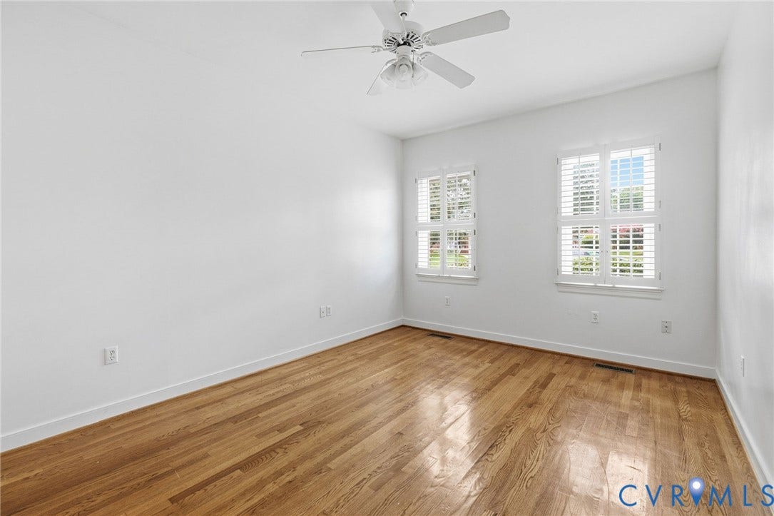 Hardwood flooring, white walls, two windows with white plantation shutters, and a ceiling fan