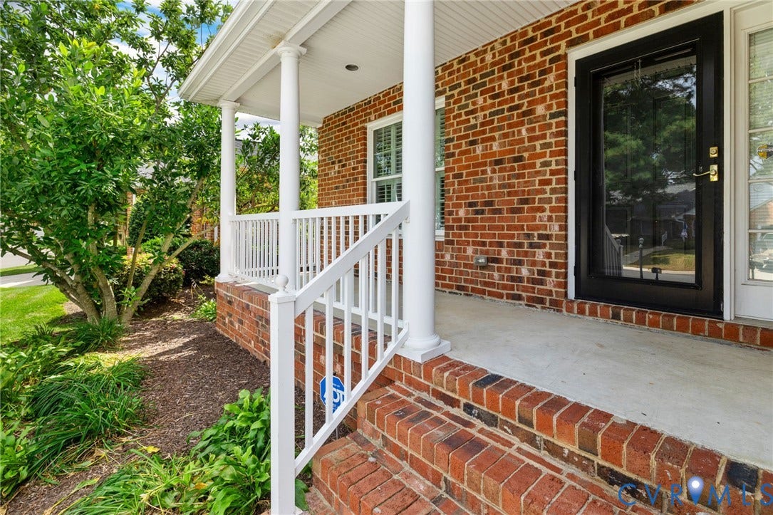 Brick exterior, covered porch with white columns, white railing, concrete porch floor, and a black full-glass entry door