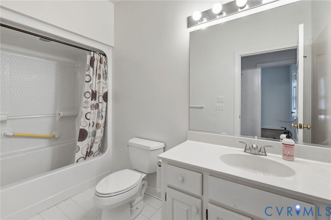 Hall bathroom with white tile flooring, white vanity with integrated sink, chrome faucet, wall-mounted mirror, and a bathtub with shower