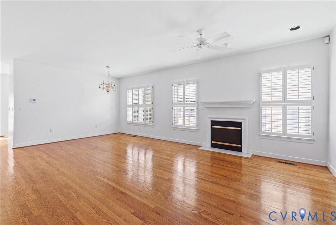Hardwood flooring throughout, white plantation shutters, white fireplace with black hearth, white ceiling fan, and chandelier