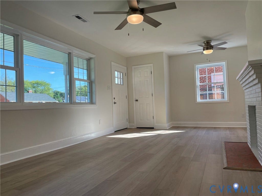 2315 Dee Kay Drive, Henrico, VA 23228 Wood-finish flooring, white trim throughout, large windows, two ceiling fans with integrated lighting, and a painted brick fireplace