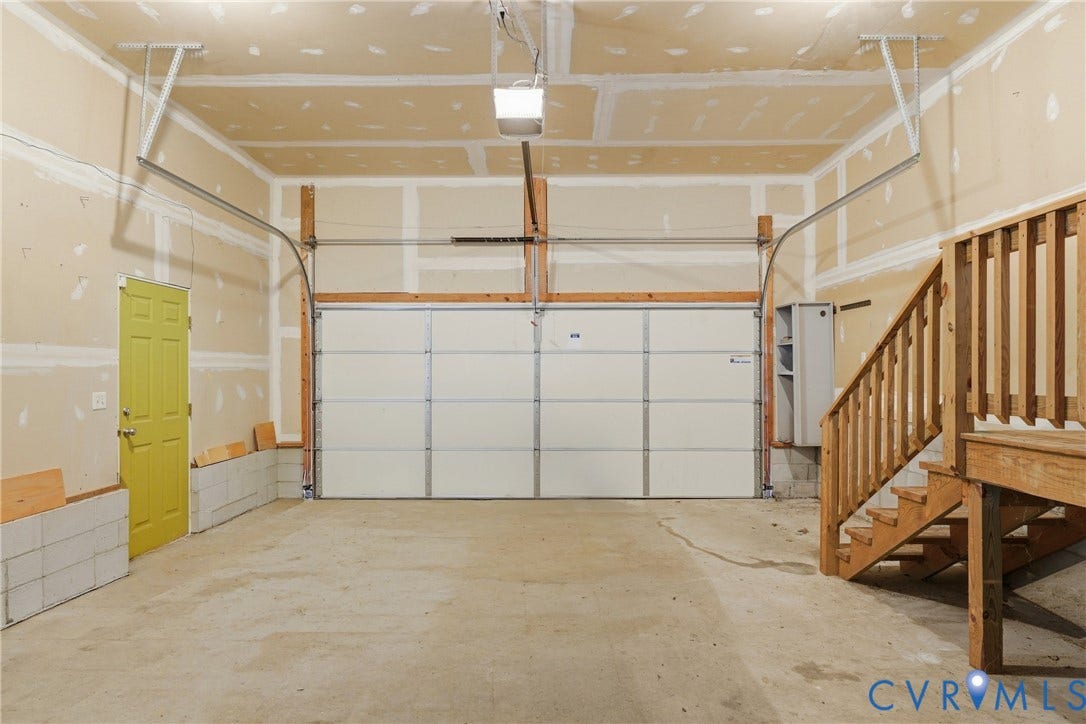 Spacious garage featuring a concrete floor, overhead lighting, and an unfinished wood staircase with railing