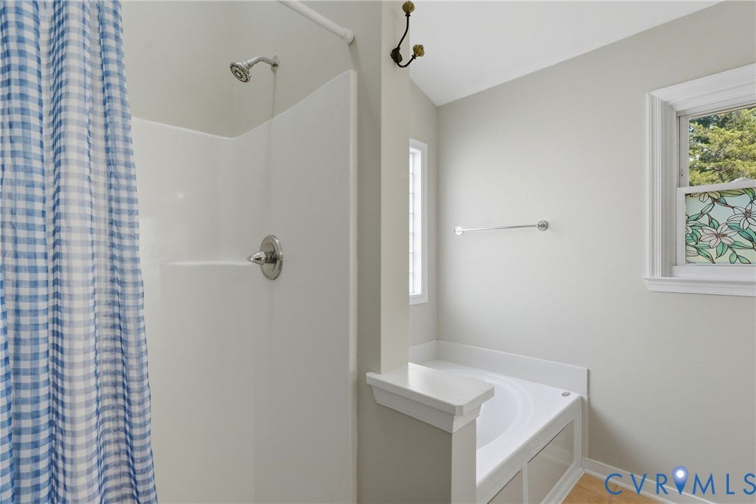 Shower and bathtub combination with white surround, polished chrome fixtures, and a stained-glass window accent