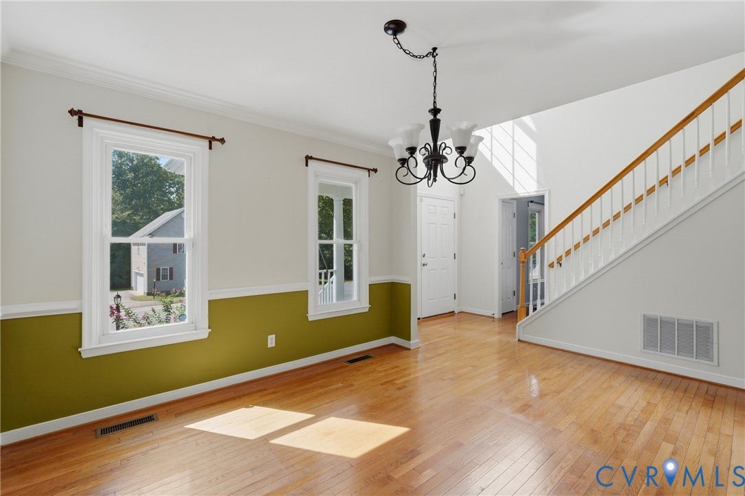 Hardwood flooring, painted walls, two large windows, staircase with wood handrail, and a decorative chandelier