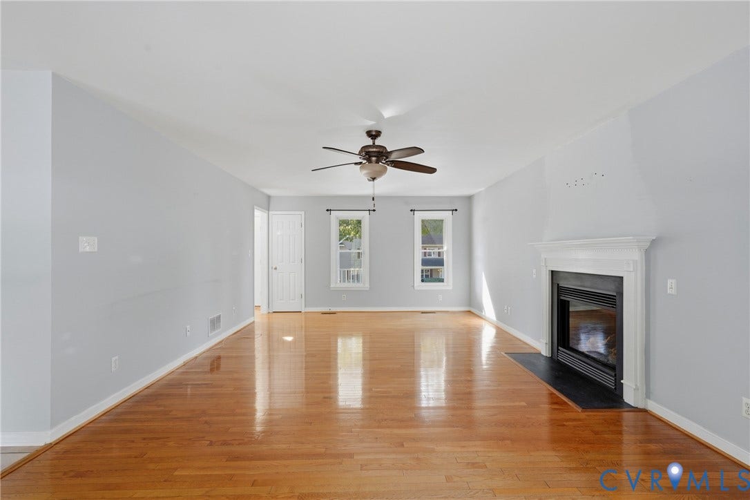 Hardwood flooring, a ceiling fan, a fireplace with a white mantel, and two windows with white trim