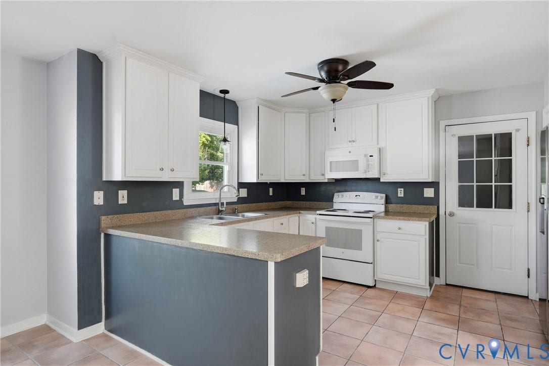White cabinetry with crown molding, light-toned countertops, white appliances, ceiling fan with light fixture, and a paneled door with glass inserts