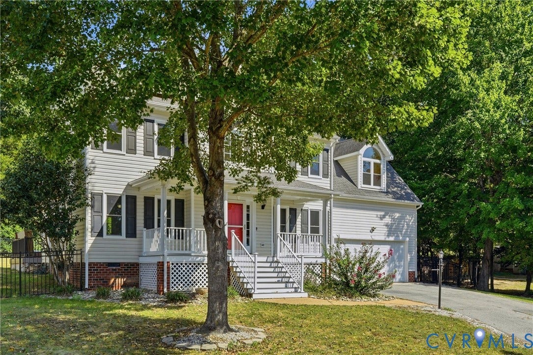 Two-story residence featuring white siding, a covered front porch with white railings, a prominent red front door, and an attached garage with a paved driveway