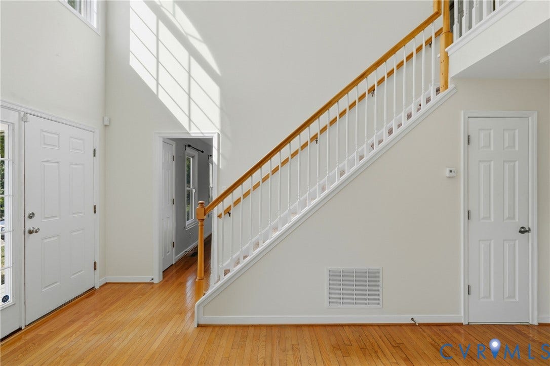 Vaulted ceiling foyer featuring a paneled entry door with sidelights, wood-finish flooring, and a staircase with wood handrails