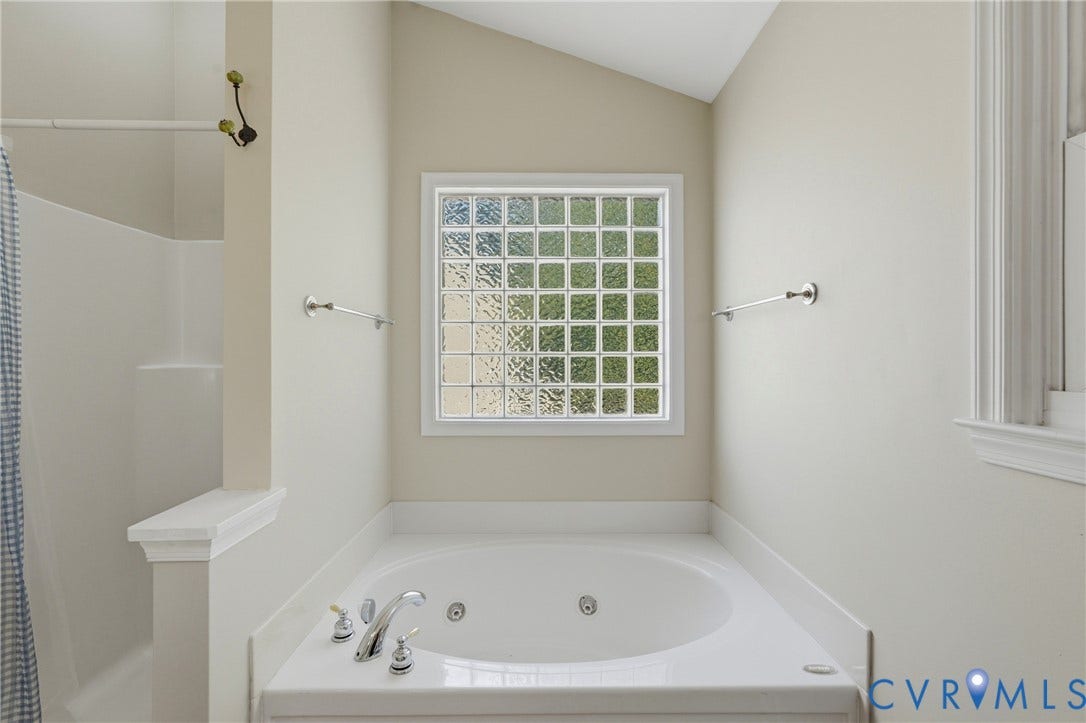 Freestanding tub with polished chrome fixtures, glass block window, and adjacent shower enclosure with built-in shelving