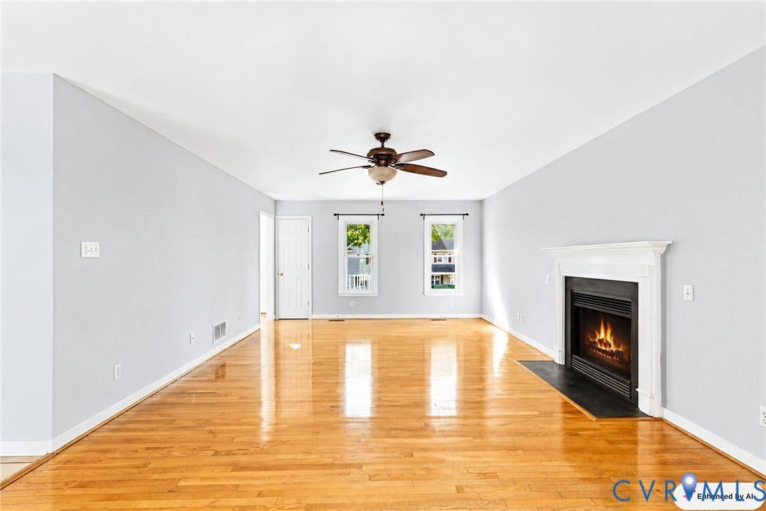 Hardwood flooring, white door, two windows, fireplace with mantel, ceiling fan