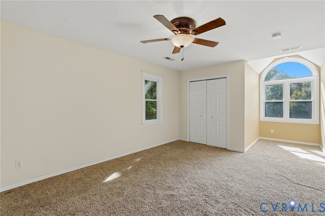 Carpeted room featuring a ceiling fan with integrated lighting, a large arched window, a standard rectangular window, and a built-in closet with bi-fold doors