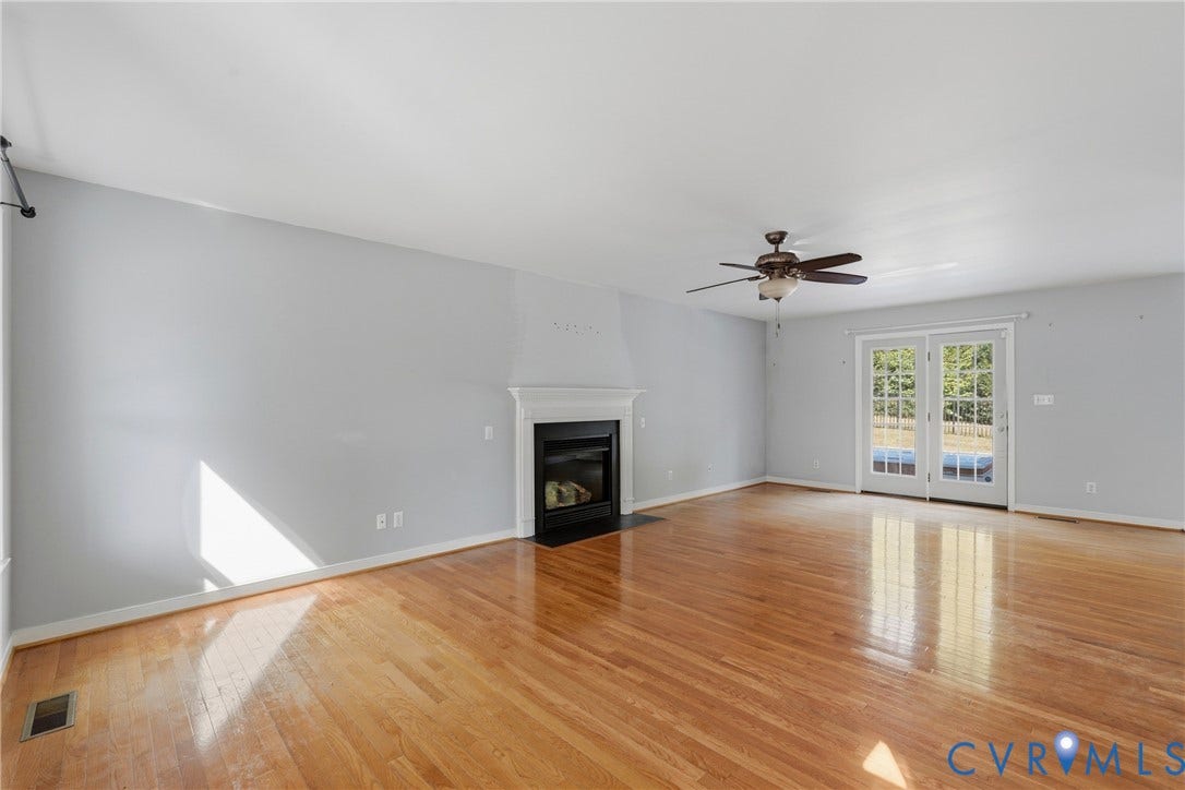 Wood-finish flooring throughout, light gray wall color, white mantel fireplace, and double French doors with transom windows