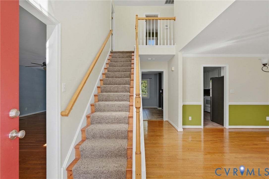 Two-story entry foyer featuring hardwood flooring, carpeted staircase with wood handrail, and a second-story landing with white balusters