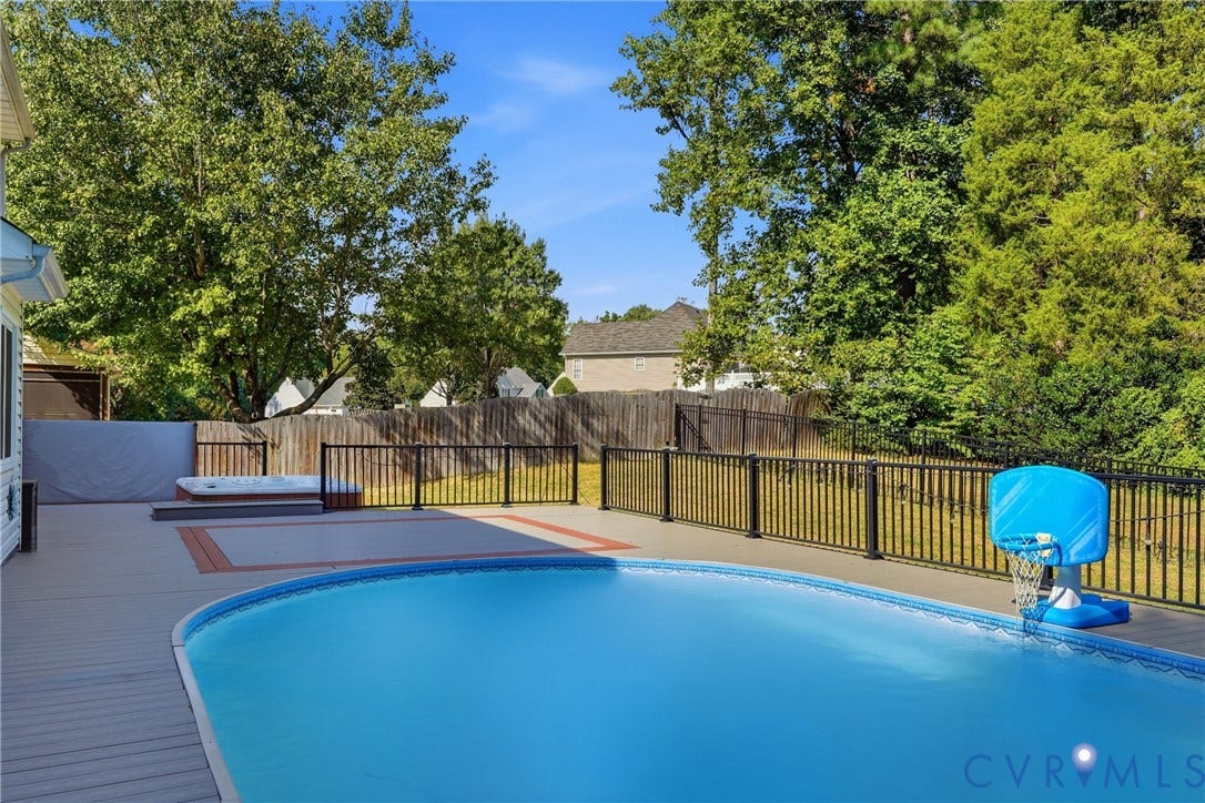 Outdoor living space featuring a built-in swimming pool, integrated spa, expansive decking, and perimeter fencing