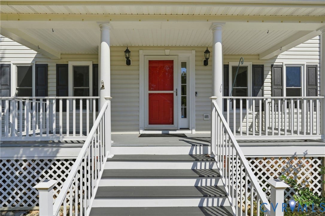 Front porch with white railings, a bright red front door, and dark shutters