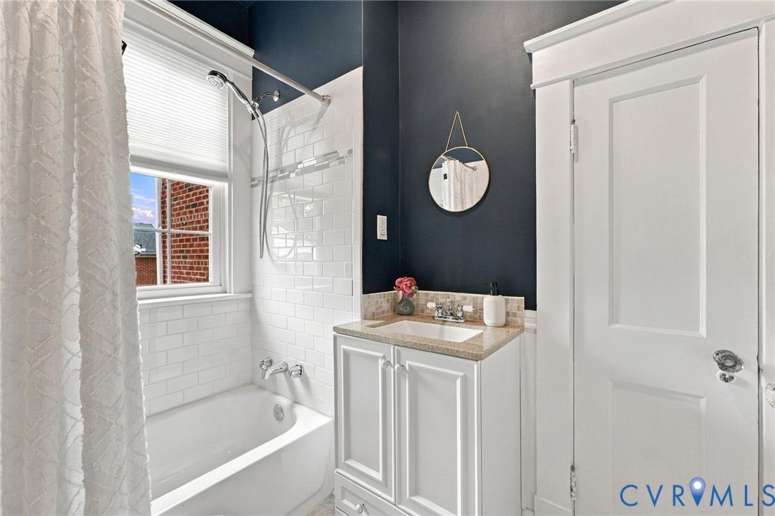 4905 Patterson Avenue, Richmond, VA 23226 Built-in bathtub with subway tile surround, window with privacy blind, vanity with integrated sink and stone countertop, and paneled door with decorative trim