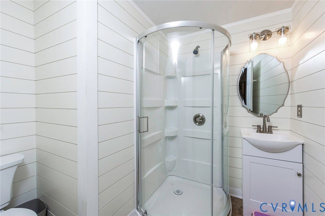 5640 Teterling Court, Lakewood Farms, Chester, VA 23831 White shiplap wall finishes, corner shower with clear glass enclosure, compact vanity with integrated sink, brushed nickel faucet, and vanity lighting fixture